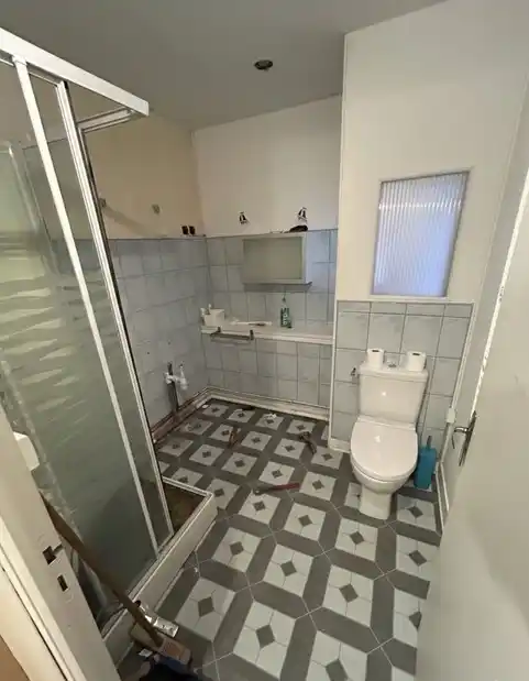 Salle de bain ancienne avec douche et WC avant rénovation, carrelage gris au sol et murs
